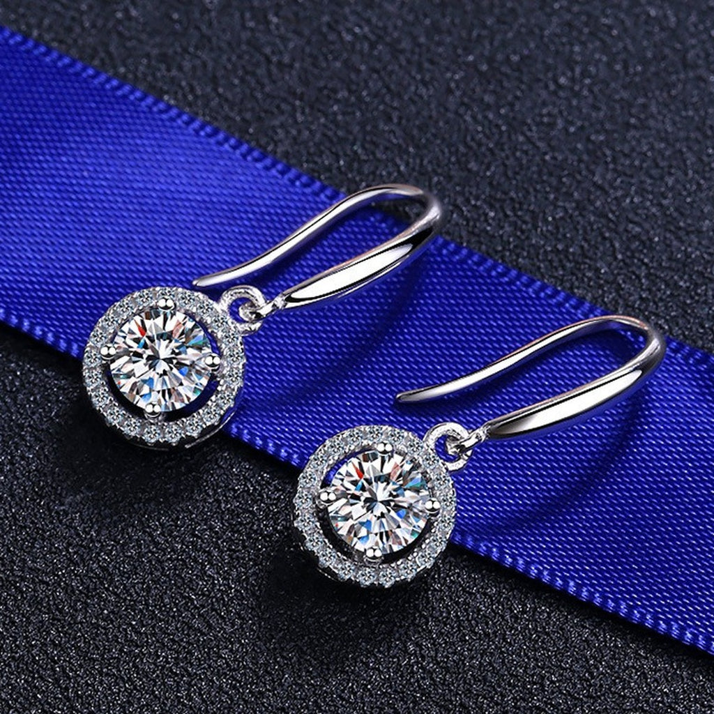 Round Halo Moissanite Hook Dangle Earrings with CZ in Rhodium-Plated S925 Sterling Silver on blue-green fabric showing angled setting view