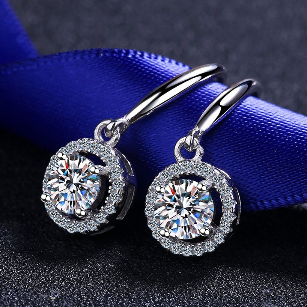 Round Halo Moissanite Hook Dangle Earrings with CZ in Rhodium-Plated S925 Sterling Silver on blue-green fabric showing side profile and stone setting