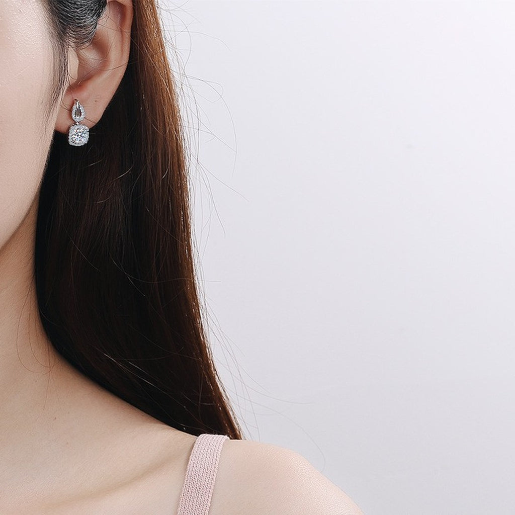 Cushion Halo Moissanite Stud Drop Earrings with CZ in Rhodium-Plated S925 Sterling Silver worn on ear by model to show scale, drop length, and everyday styling