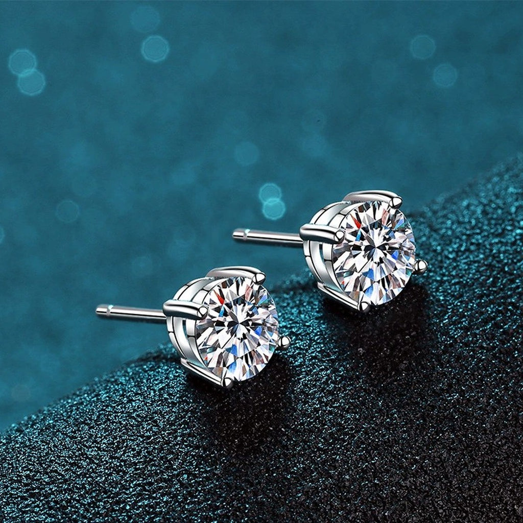 Classic Round Moissanite Stud Earrings in Rhodium-Plated S925 Sterling Silver on blue-green fabric showing angled setting view