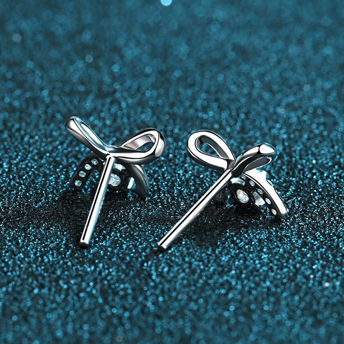 Bow Moissanite Stud Earrings with CZ in Rhodium-Plated S925 Sterling Silver on blue-green fabric showing front detail