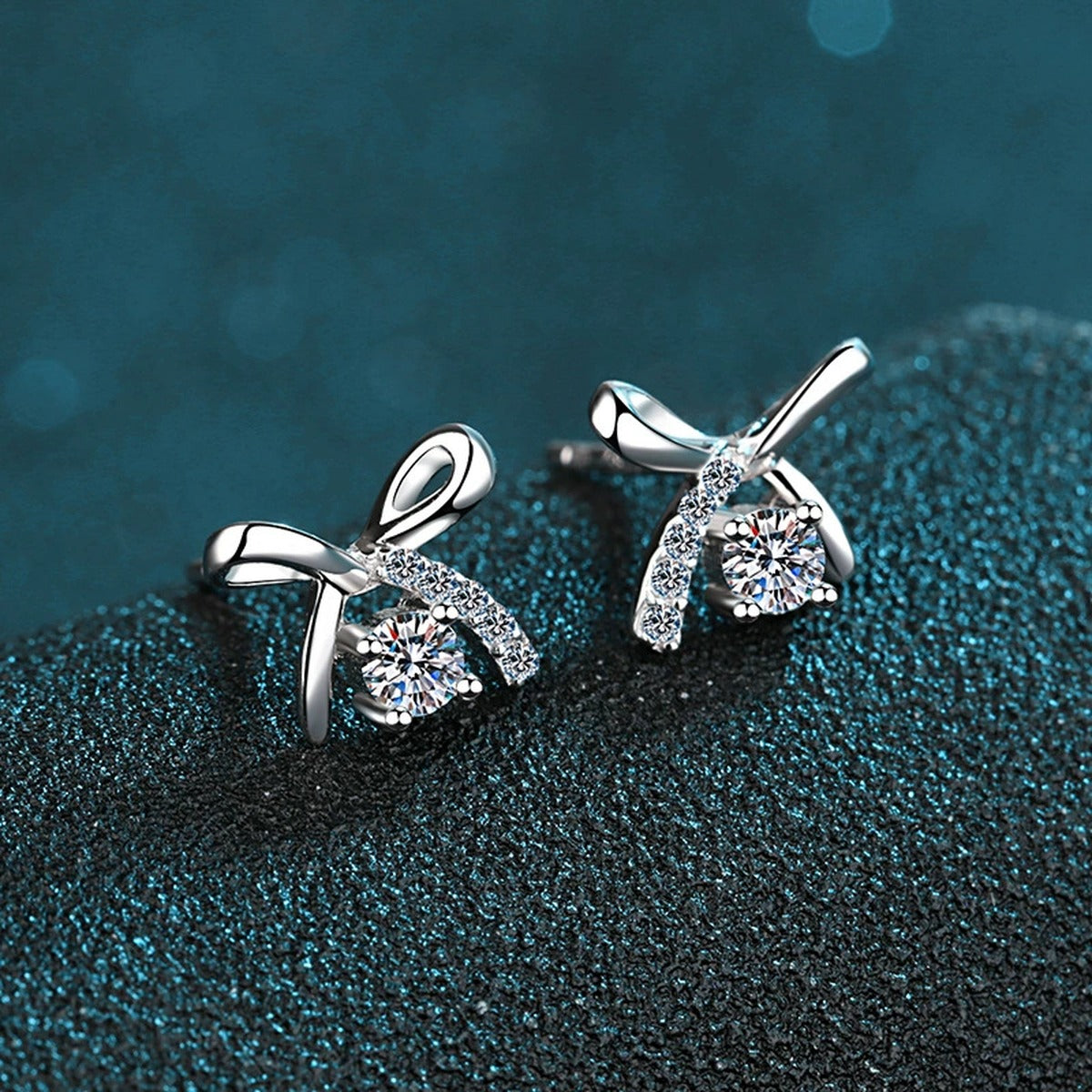 Bow Moissanite Stud Earrings with CZ in Rhodium-Plated S925 Sterling Silver on blue-green fabric showing angled setting view