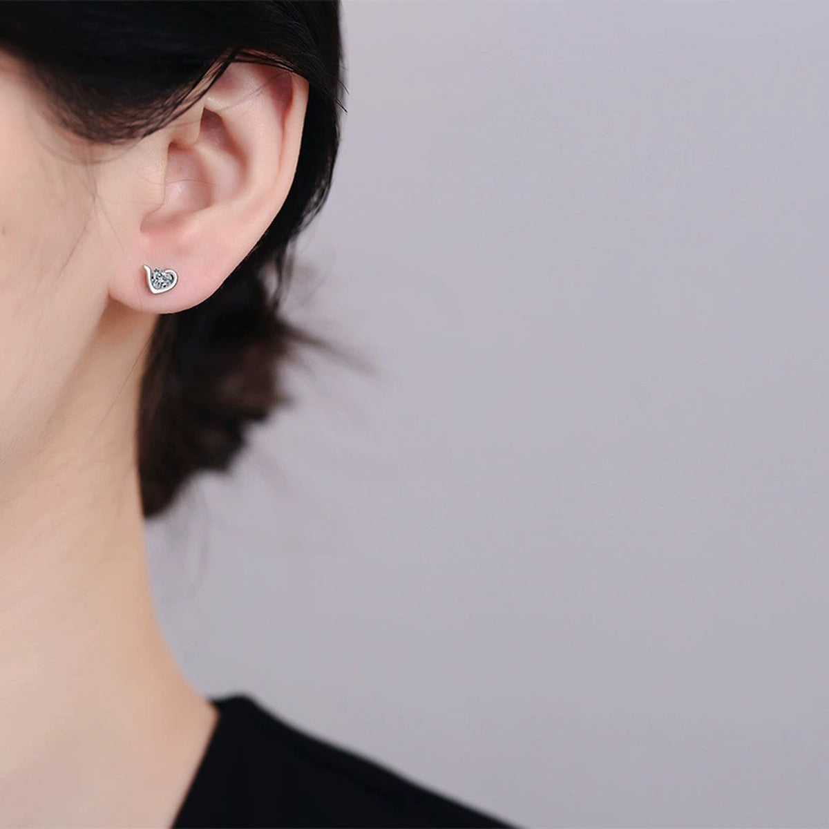 Heart Moissanite Stud Earrings in Rhodium-Plated S925 sterling silver worn on ear by model showing scale, placement, and stud earrings styling