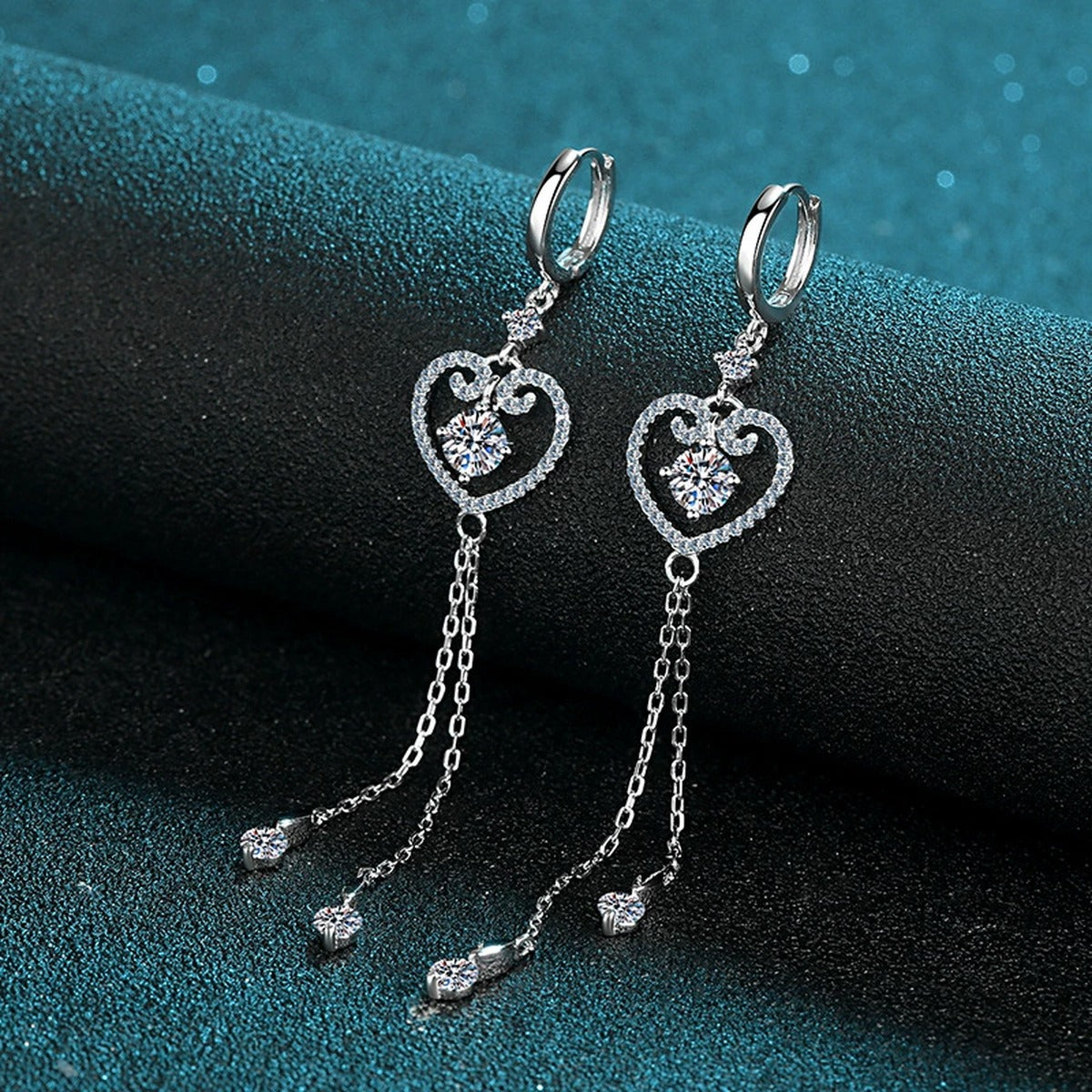 Heart Moissanite Hoop Dangle Earrings with CZ in Rhodium-Plated S925 Sterling Silver on blue-green fabric showing angled setting view