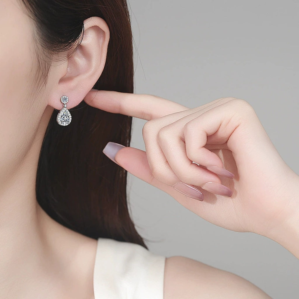 Pear Cut Moissanite Stud Drop Earrings with CZ in Rhodium-Plated S925 sterling silver worn on ear by model showing scale, placement, and stud earrings styling