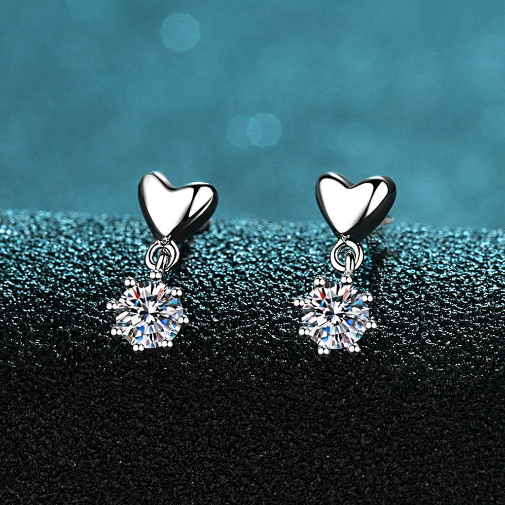 Heart Moissanite Stud Dangle Earrings in Rhodium-Plated S925 Sterling Silver on blue-green fabric showing angled setting view