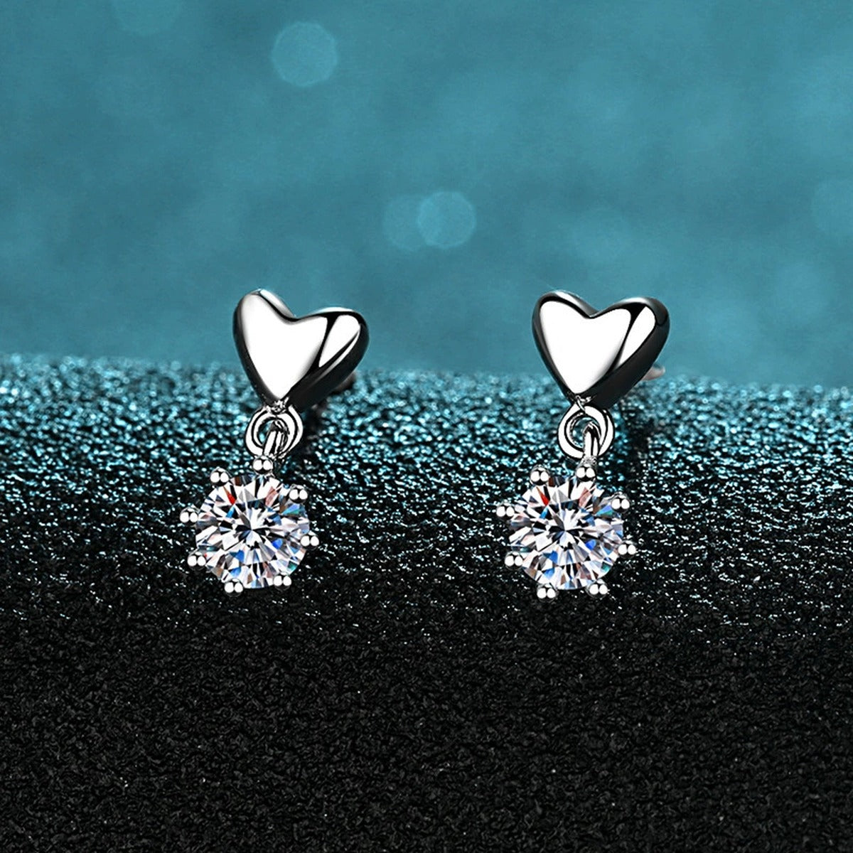 Heart Moissanite Stud Dangle Earrings in Rhodium-Plated S925 Sterling Silver on blue-green fabric showing angled setting view