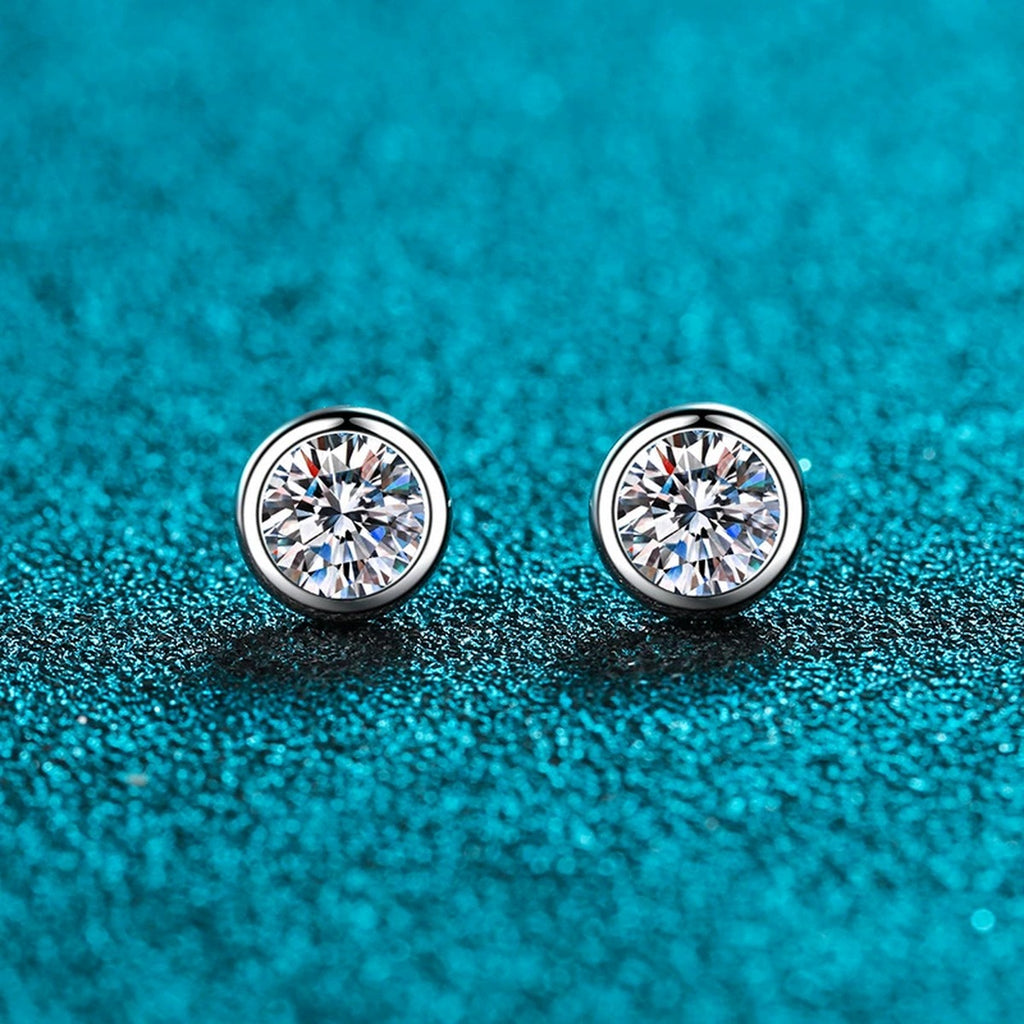 Bezel Round Moissanite Stud Earrings in Rhodium-Plated S925 Sterling Silver on blue-green fabric showing front detail