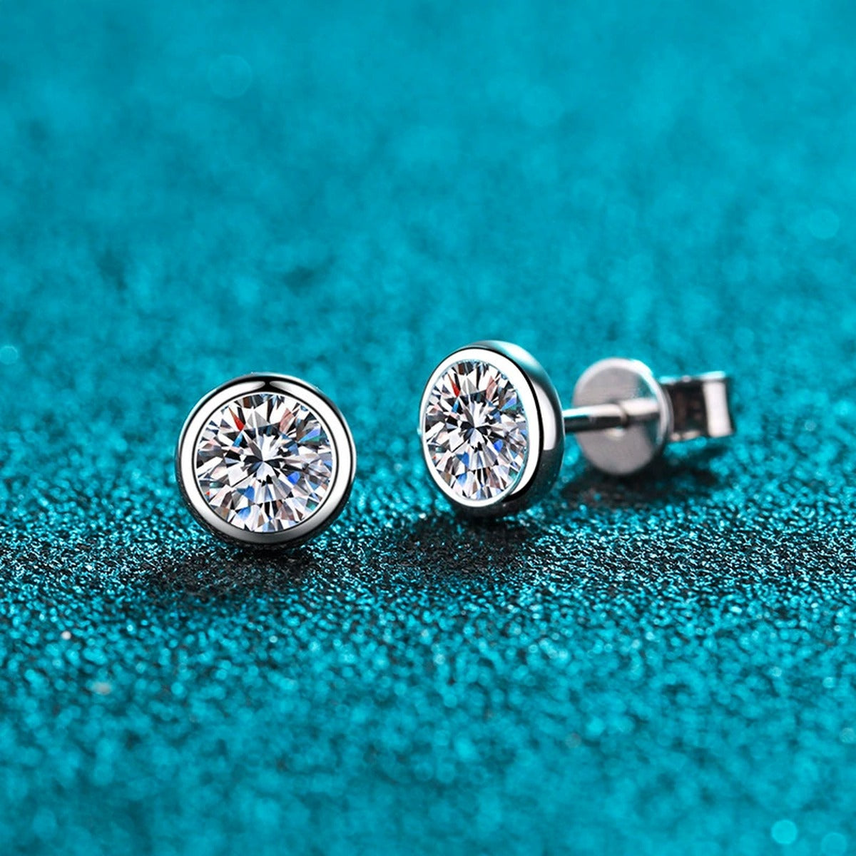 Bezel Round Moissanite Stud Earrings in Rhodium-Plated S925 Sterling Silver on blue-green fabric showing side profile and stone setting