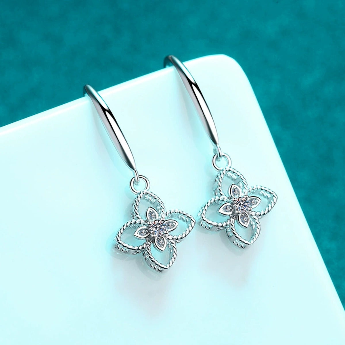 Floral Moissanite Hook Dangle Earrings in Rhodium-Plated S925 Sterling Silver on blue-green fabric showing angled setting view