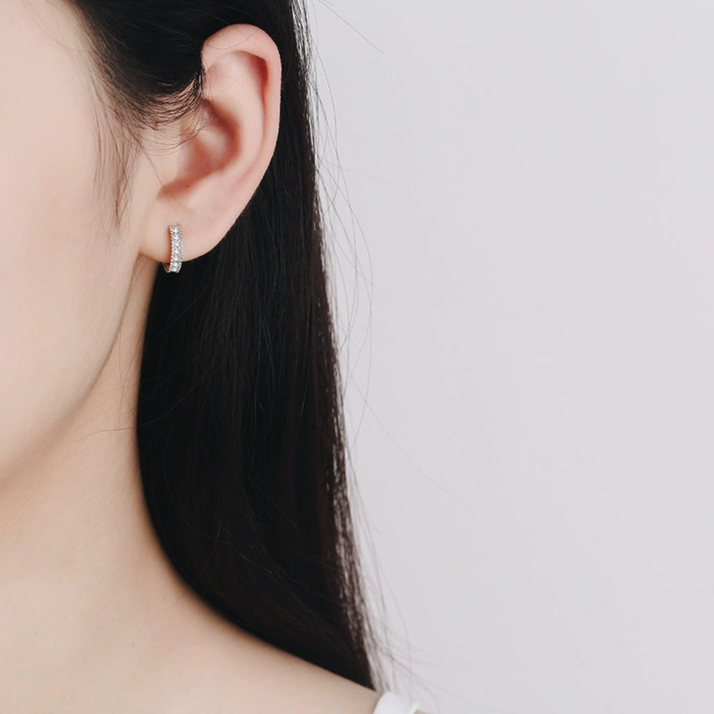 Pavé Moissanite Huggie Hoop Earrings in Rhodium-Plated S925 sterling silver worn on ear by model showing scale, placement, and huggie hoop earrings styling