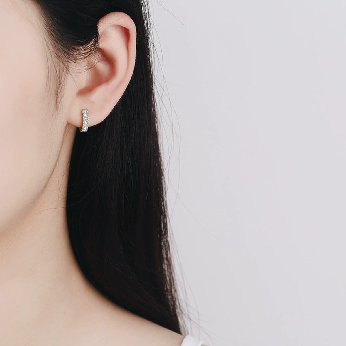 Pavé Moissanite Huggie Hoop Earrings in Rhodium-Plated S925 sterling silver worn on ear by model showing scale, placement, and huggie hoop earrings styling