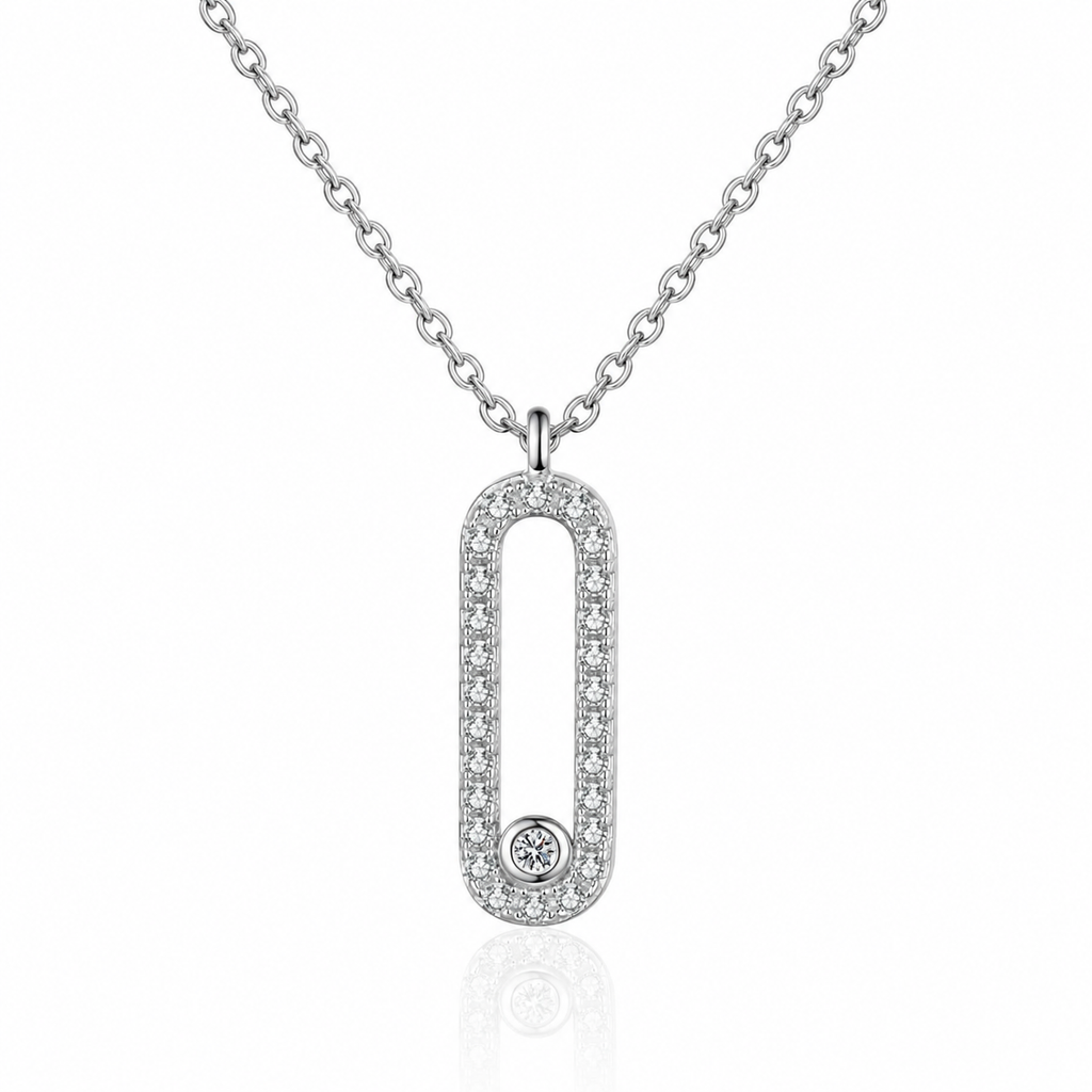 A silver-toned oval pendant necklace with a border of small clear stones and a single round stone at the bottom, shown on a white background with a faint reflection.