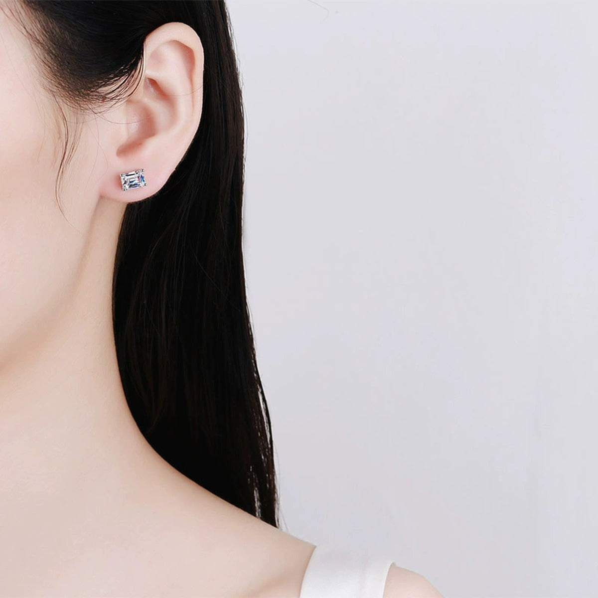 Emerald and Radiant Cut Moissanite Stud Earrings in Rhodium-Plated S925 sterling silver worn on ear by model showing scale, placement, and stud earrings styling