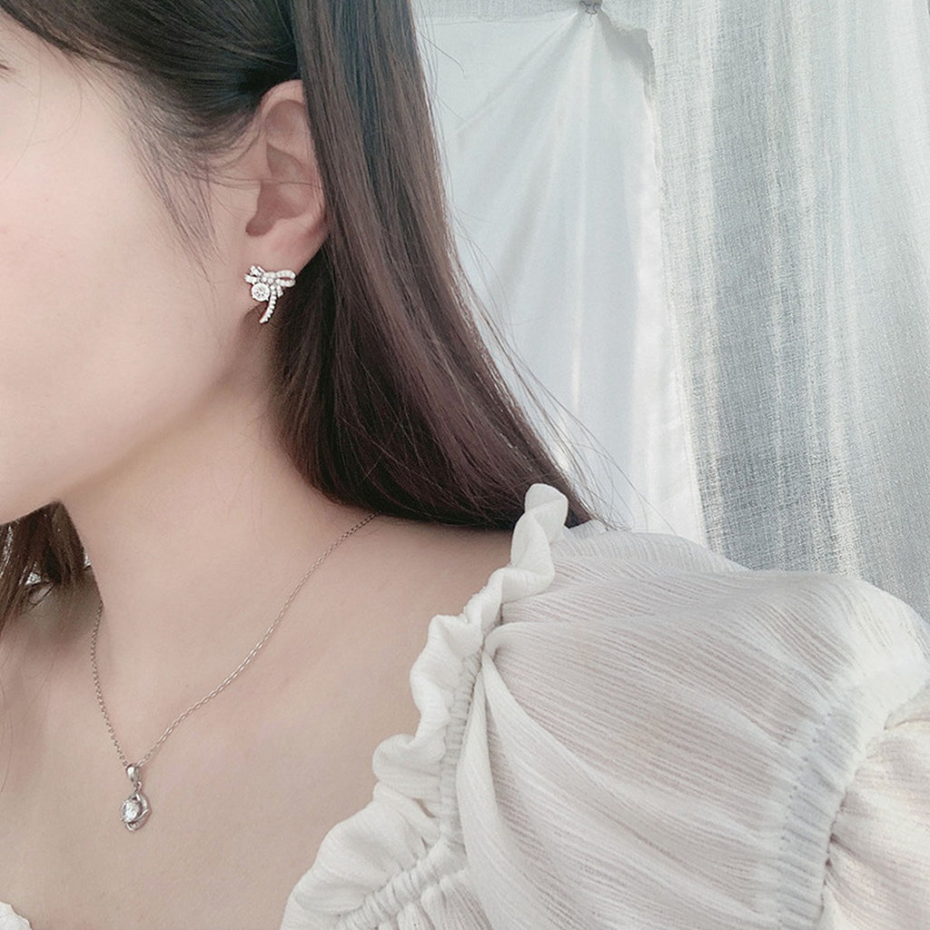 Ribbon Bow Round Moissanite Stud Earrings with CZ in White Gold-Plated S925 sterling silver worn on ear by model showing scale, placement, and stud earrings styling