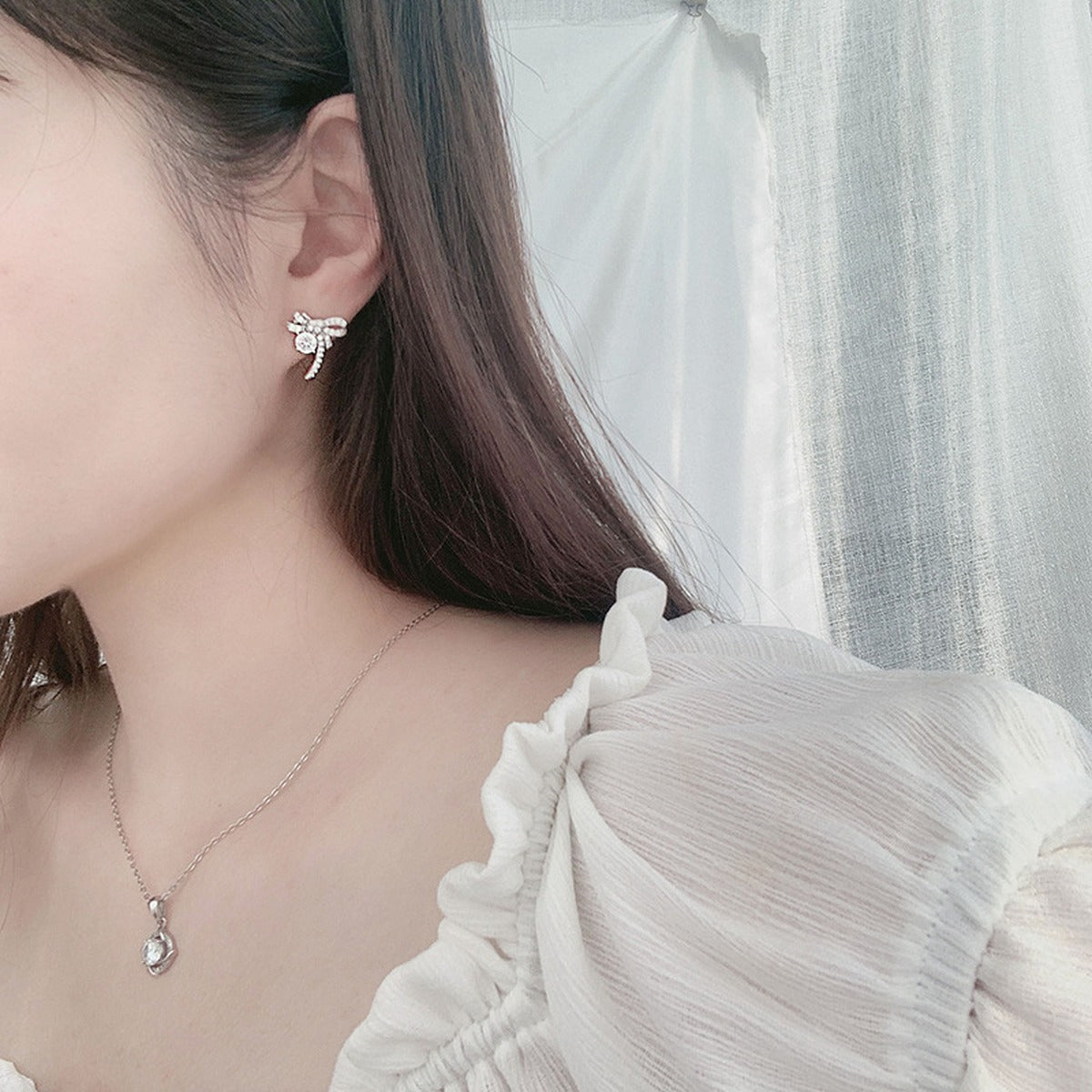 Ribbon Bow Round Moissanite Stud Earrings with CZ in White Gold-Plated S925 sterling silver worn on ear by model showing scale, placement, and stud earrings styling