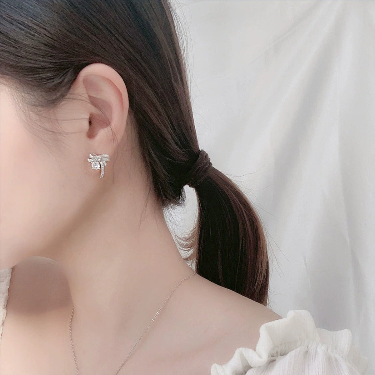 Ribbon Bow Round Moissanite Stud Earrings with CZ in White Gold-Plated S925 sterling silver worn on ear by model showing scale, placement, and stud earrings styling