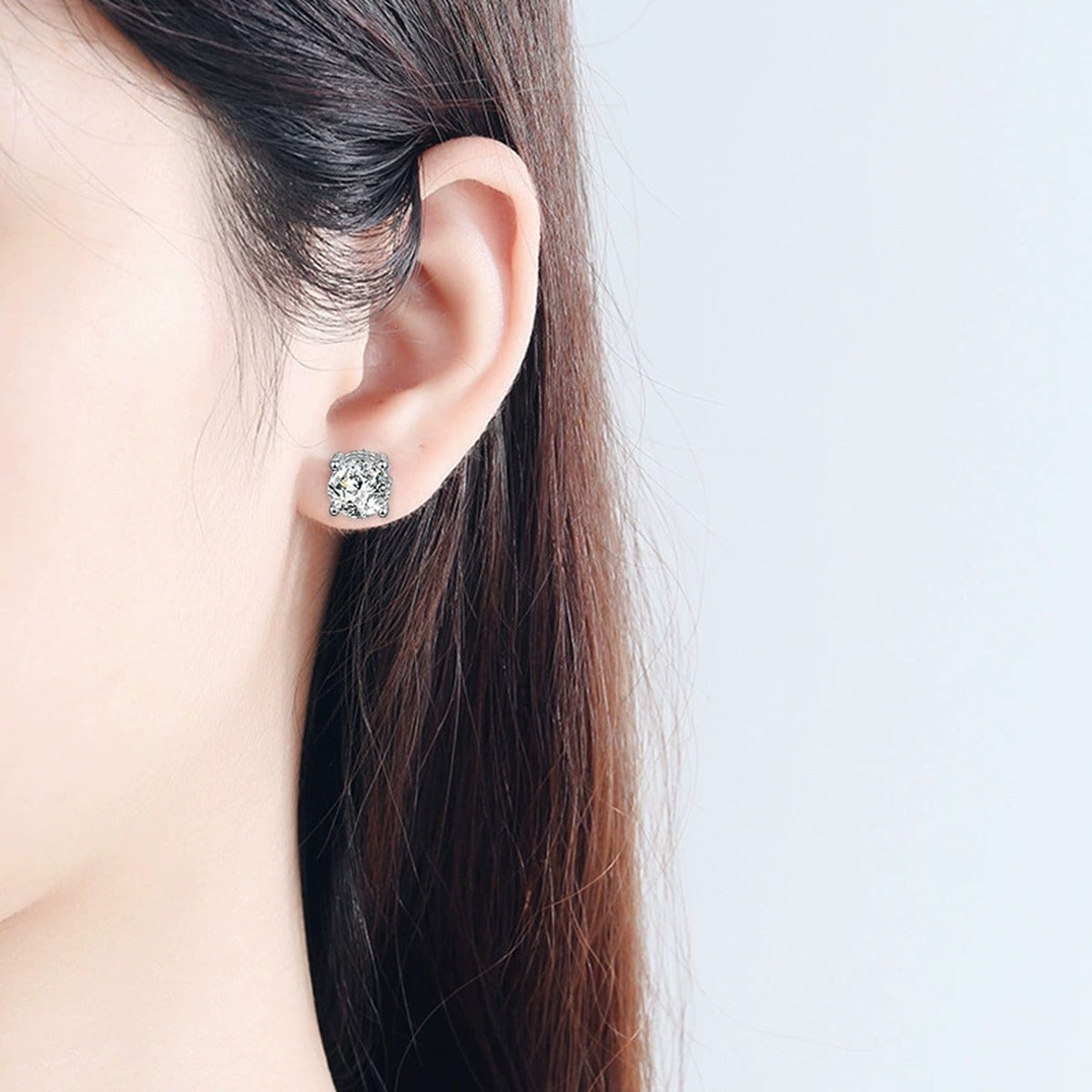 Four-Prong Round Moissanite Solitaire Stud Earrings in White Gold-Plated S925 sterling silver worn on ear by model showing scale, placement, and stud earrings styling