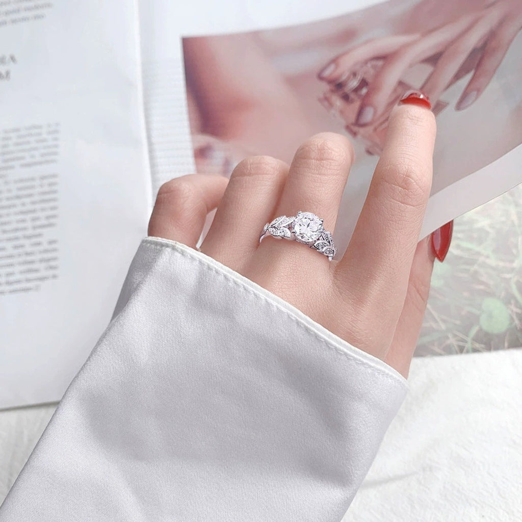 Leaf Motif Four-Prong Round Moissanite Engagement Ring with CZ worn on hand to show scale, band width, and ring profile