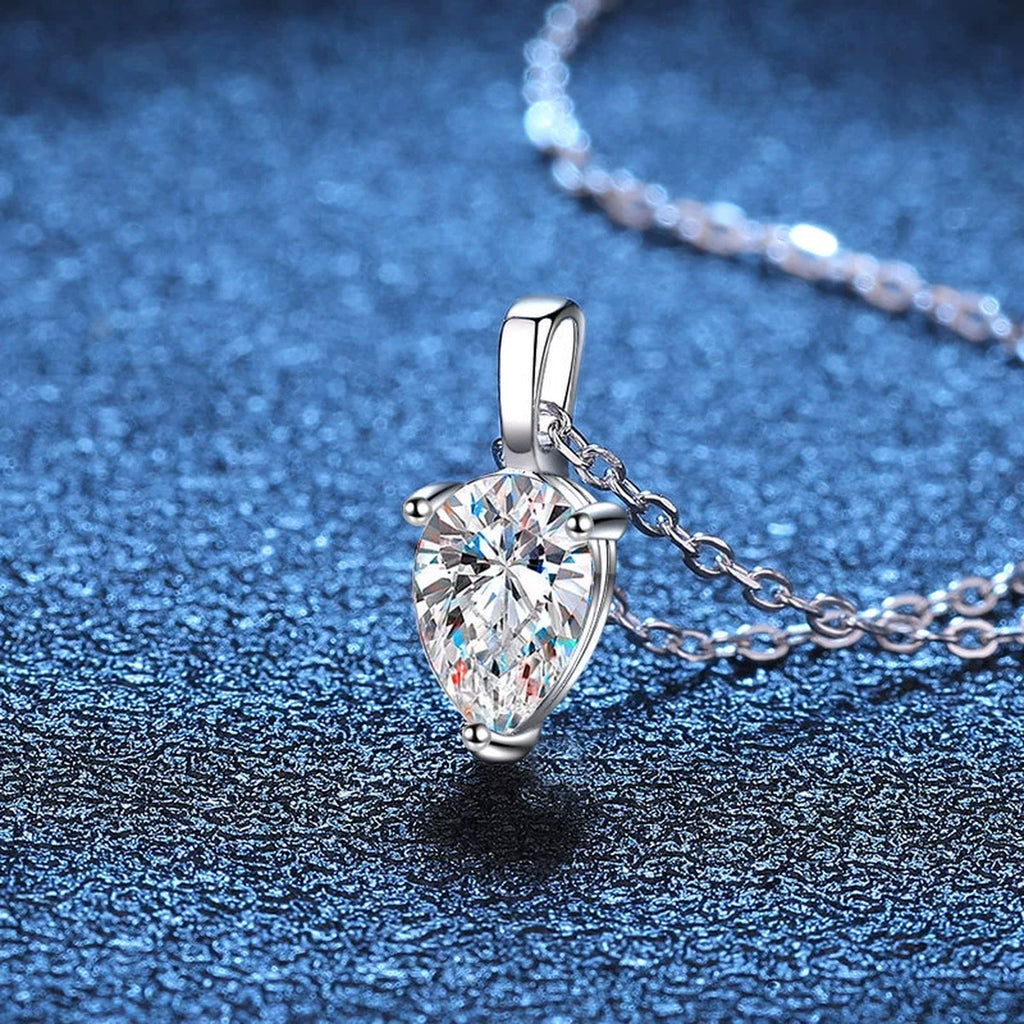 Pear moissanite pendant necklace on blue textured background