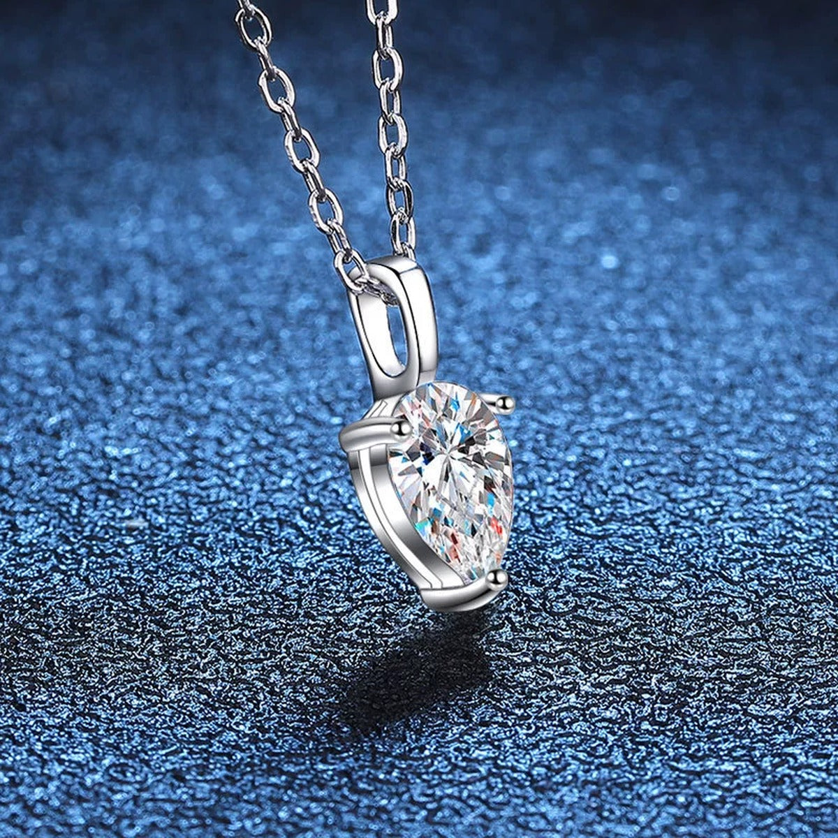 Angled view of pear moissanite pendant necklace on blue textured background