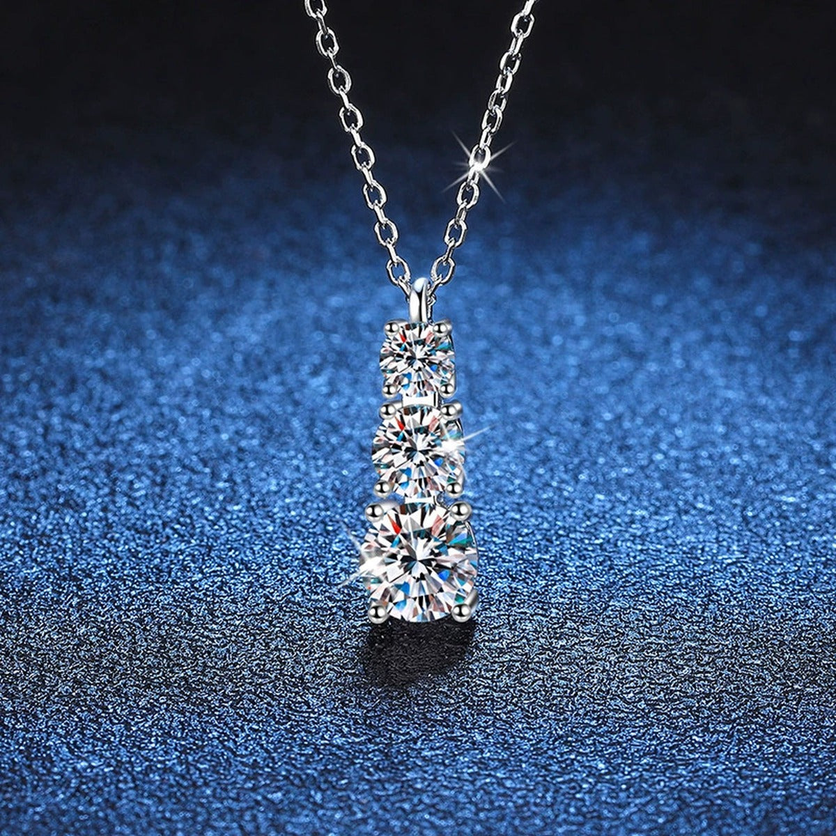 Graduated Three-Stone Moissanite Drop Necklace in Platinum-Plated S925 Sterling Silver blue background close-up view