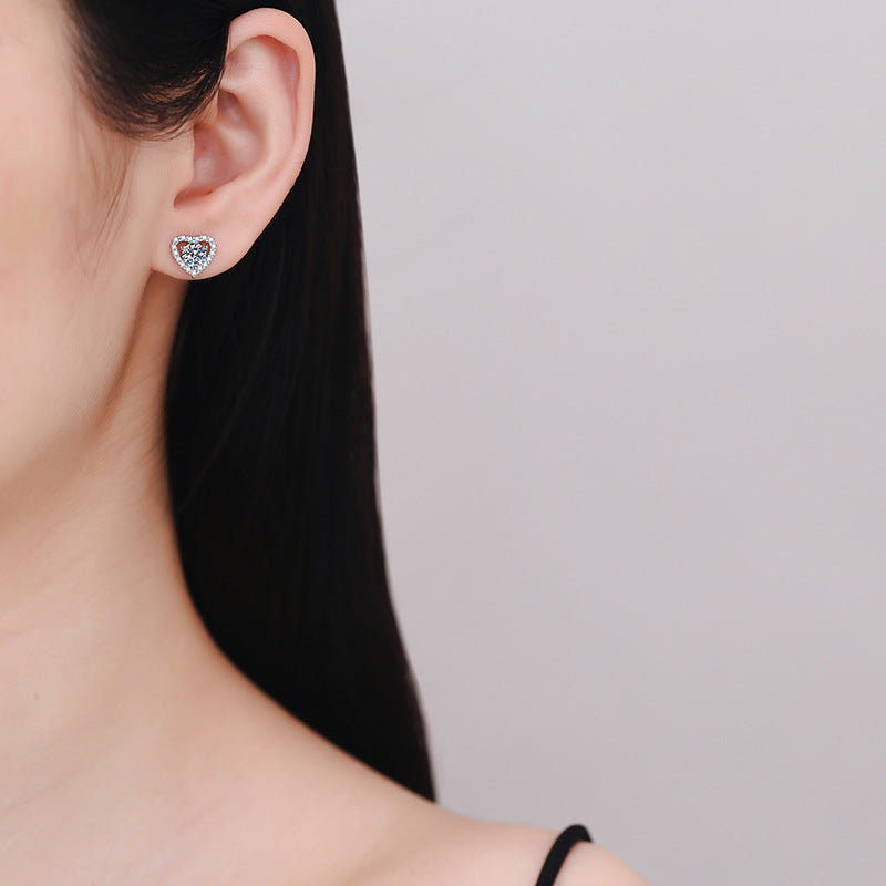 Close-up of a person wearing a heart-shaped earring on a plain background