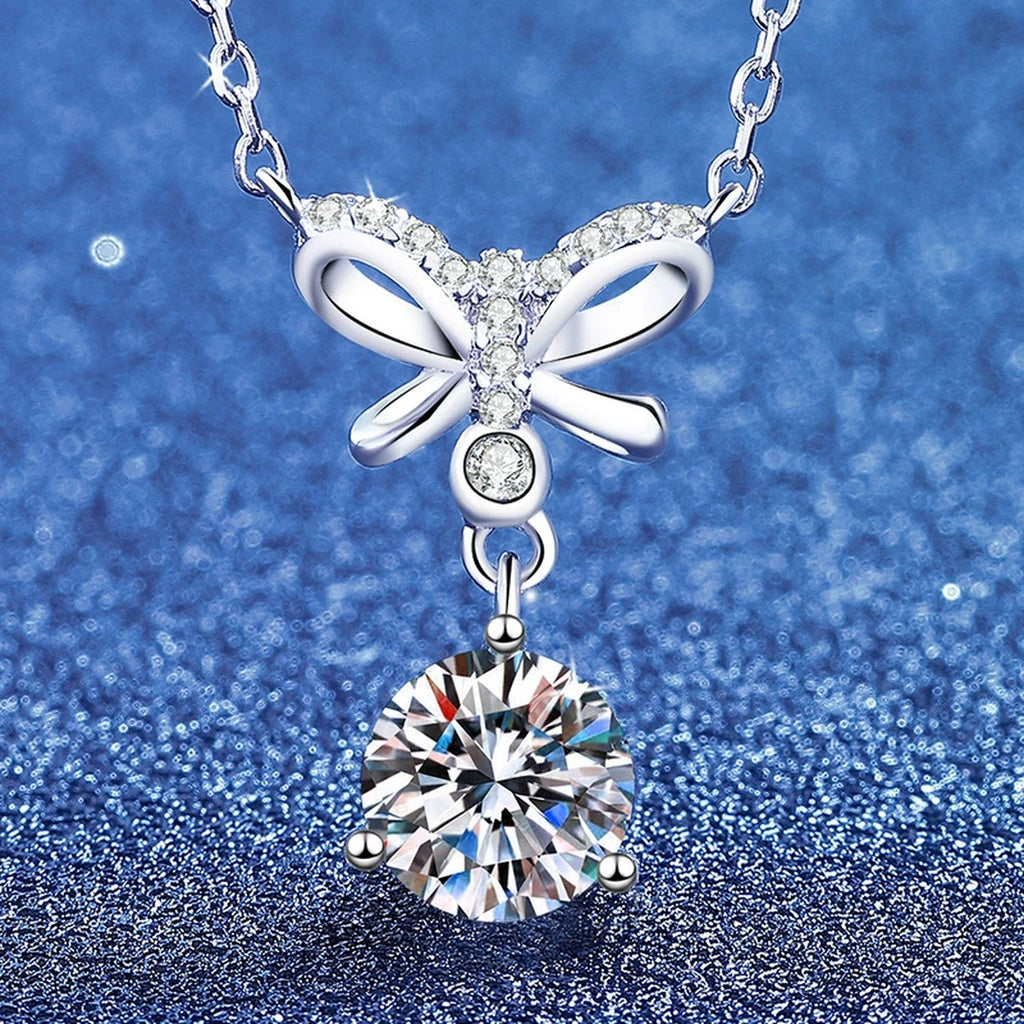 Front view of bow round moissanite pendant necklace on blue textured background