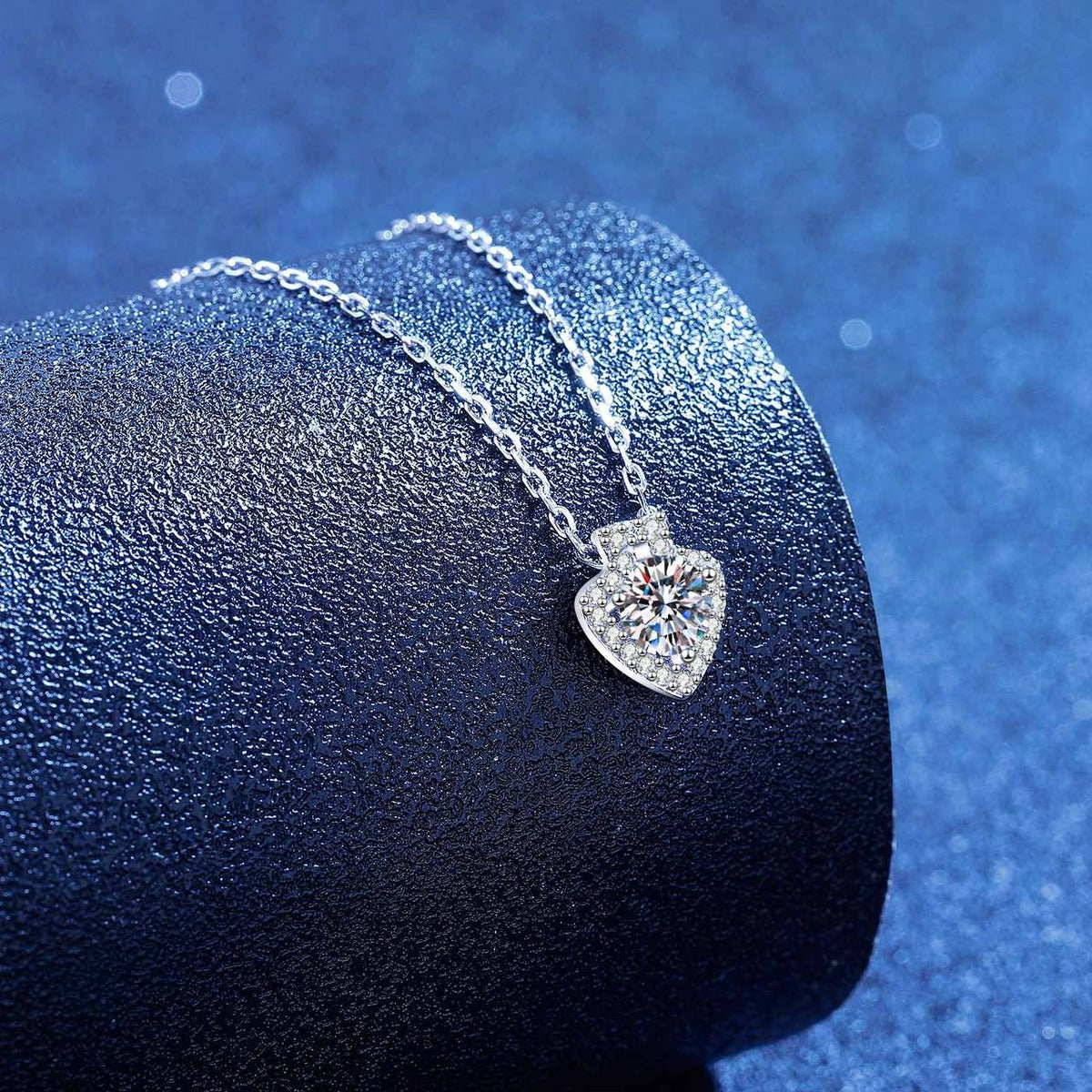 Platinum-plated heart moissanite pendant necklace styled on blue display