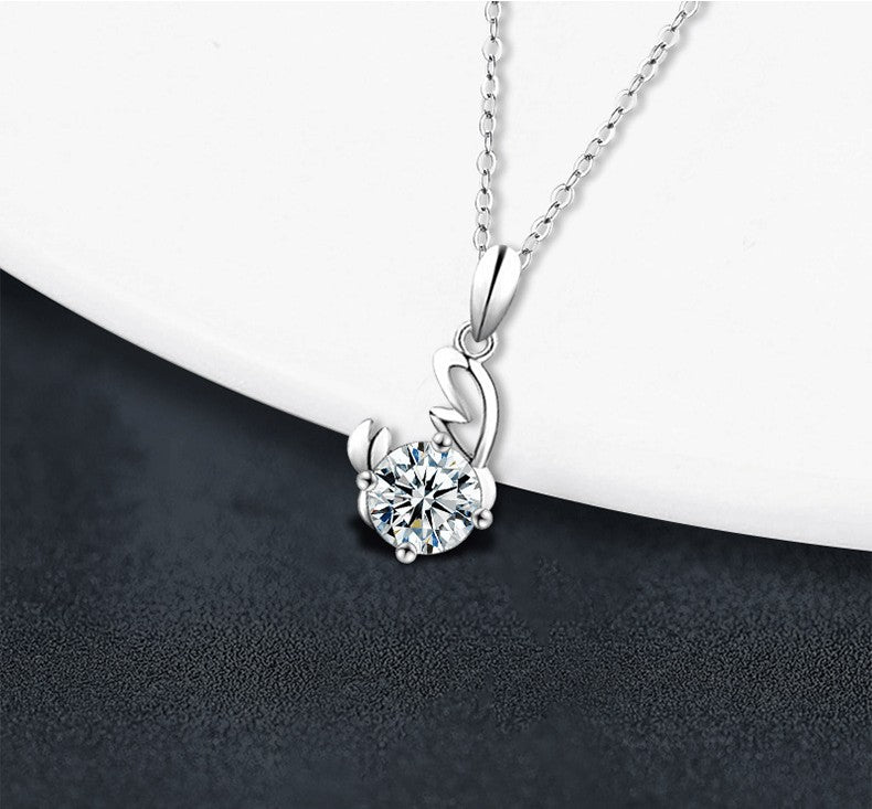 A silver pendant necklace with a clear round-cut gemstone in a prong setting, hanging from a delicate silver chain against a split white and dark gray background.