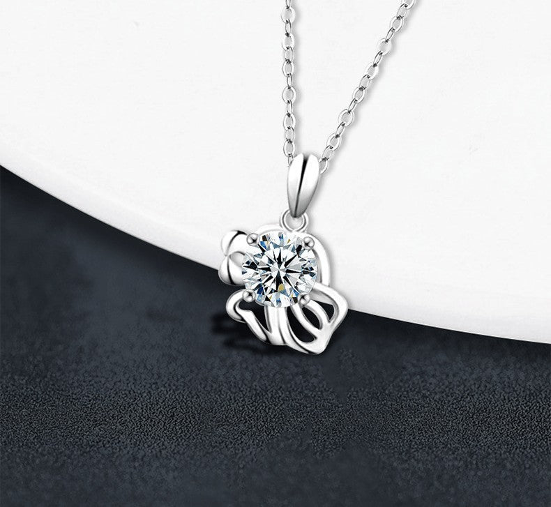 A silver pendant necklace with a clear round-cut gemstone in a prong setting, hanging from a delicate silver chain against a split white and dark gray background.