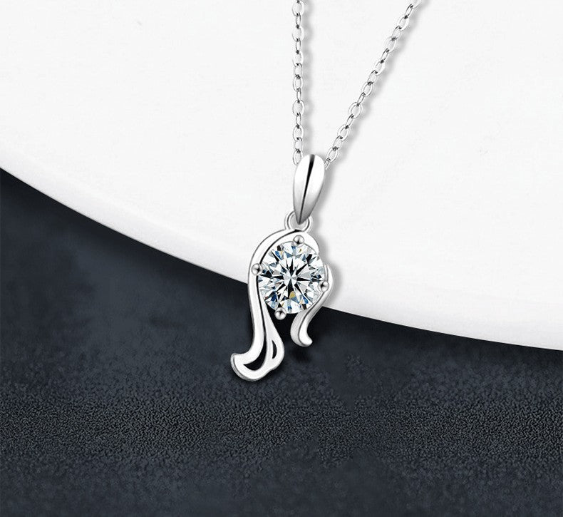 A silver pendant necklace with a clear round-cut gemstone in a prong setting, hanging from a delicate silver chain against a split white and dark gray background.