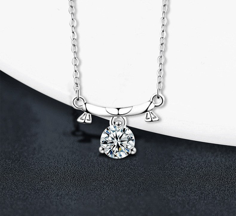 A silver pendant necklace with a clear round-cut gemstone in a prong setting, hanging from a delicate silver chain against a split white and dark gray background.