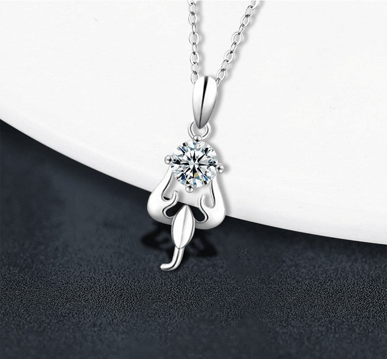 A silver pendant necklace with a clear round-cut gemstone in a prong setting, hanging from a delicate silver chain against a split white and dark gray background.