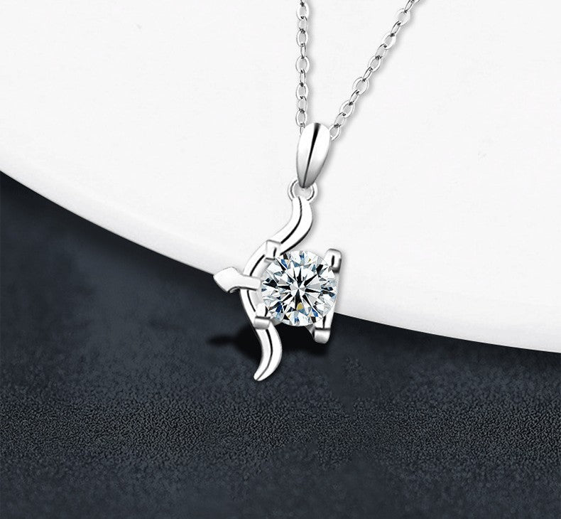 A silver pendant necklace with a clear round-cut gemstone in a prong setting, hanging from a delicate silver chain against a split white and dark gray background.