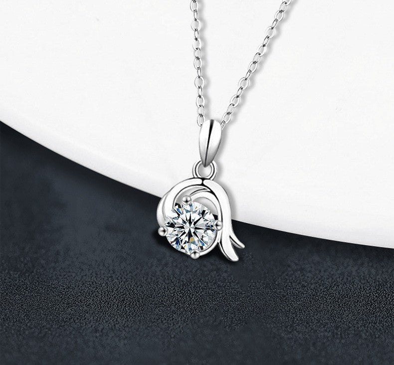 A silver pendant necklace with a clear round-cut gemstone in a prong setting, hanging from a delicate silver chain against a split white and dark gray background.